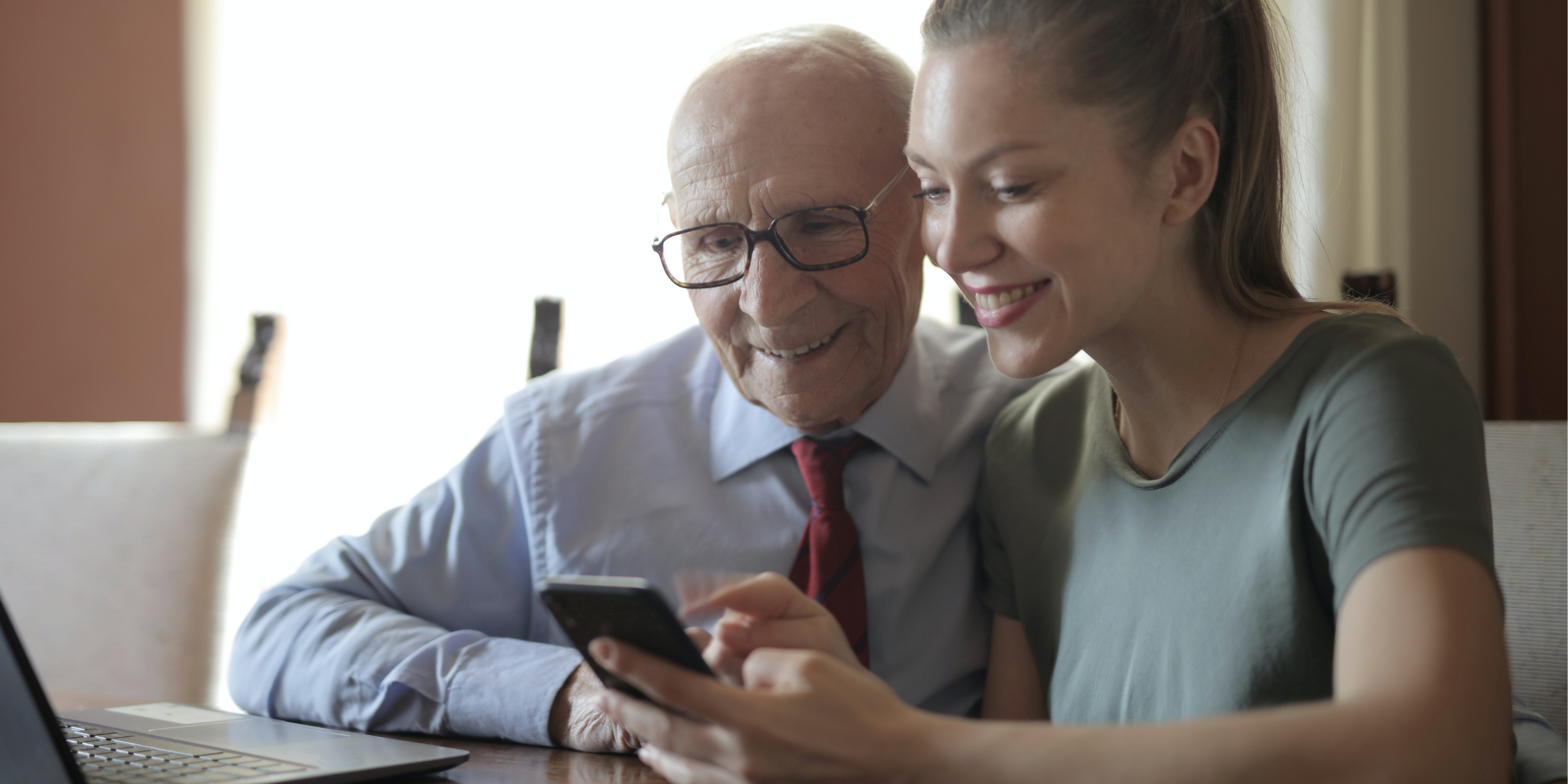 Elderly man looking at a cell phone with his daughter, helping him learn to text his provider.