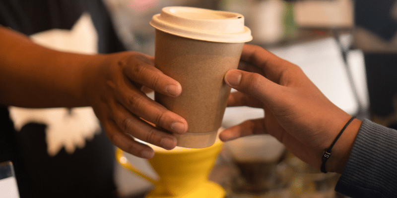 A barista hands a to-go coffee cup to a customer