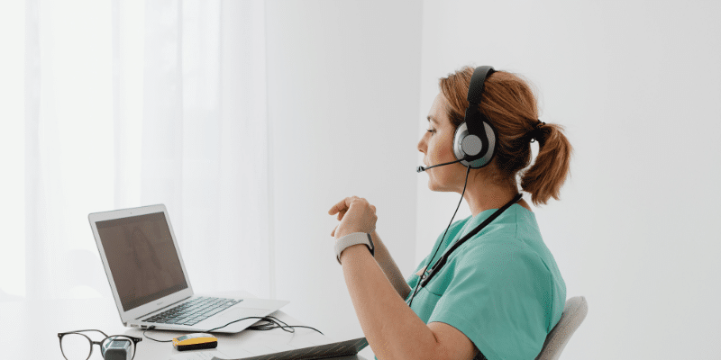 medical professional is sitting in front of a computer wearing a headset.