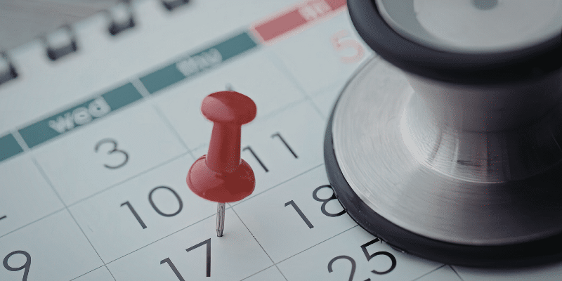 Patient scheduling calendar with a pin on day 17. A stethescope is covering the bottom of the calendar.