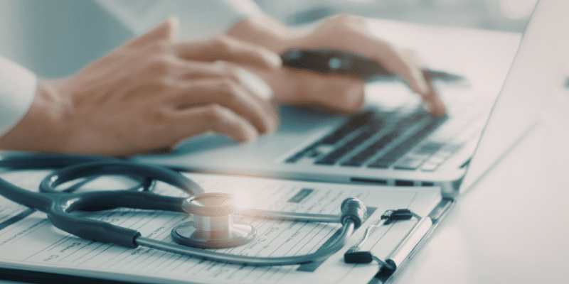 A physician types on a keyboard next to a patient chart.