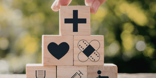Wooden blocks with healthcare symbols are stacked on a rock in a park.